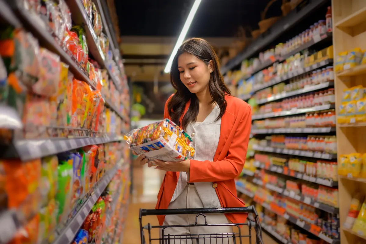 A woman checking labels in a supermarket aisle.